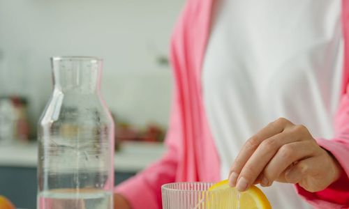 A clear glass of water with a slice of lemon next to a pitcher.